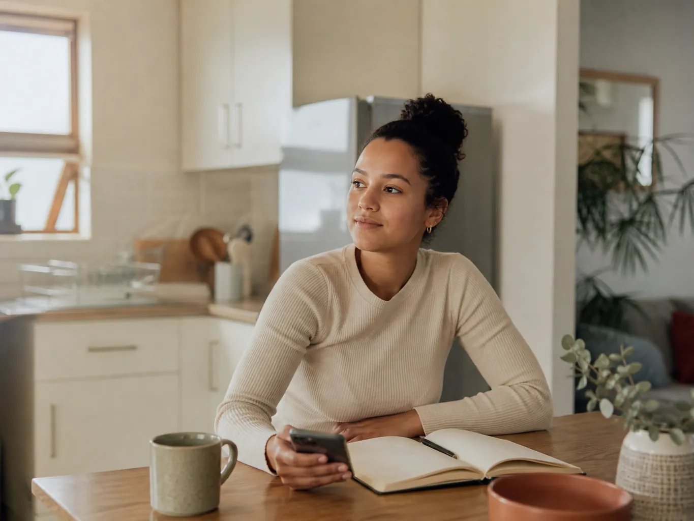 A young woman with a phone and notebook at a small kitchen table
