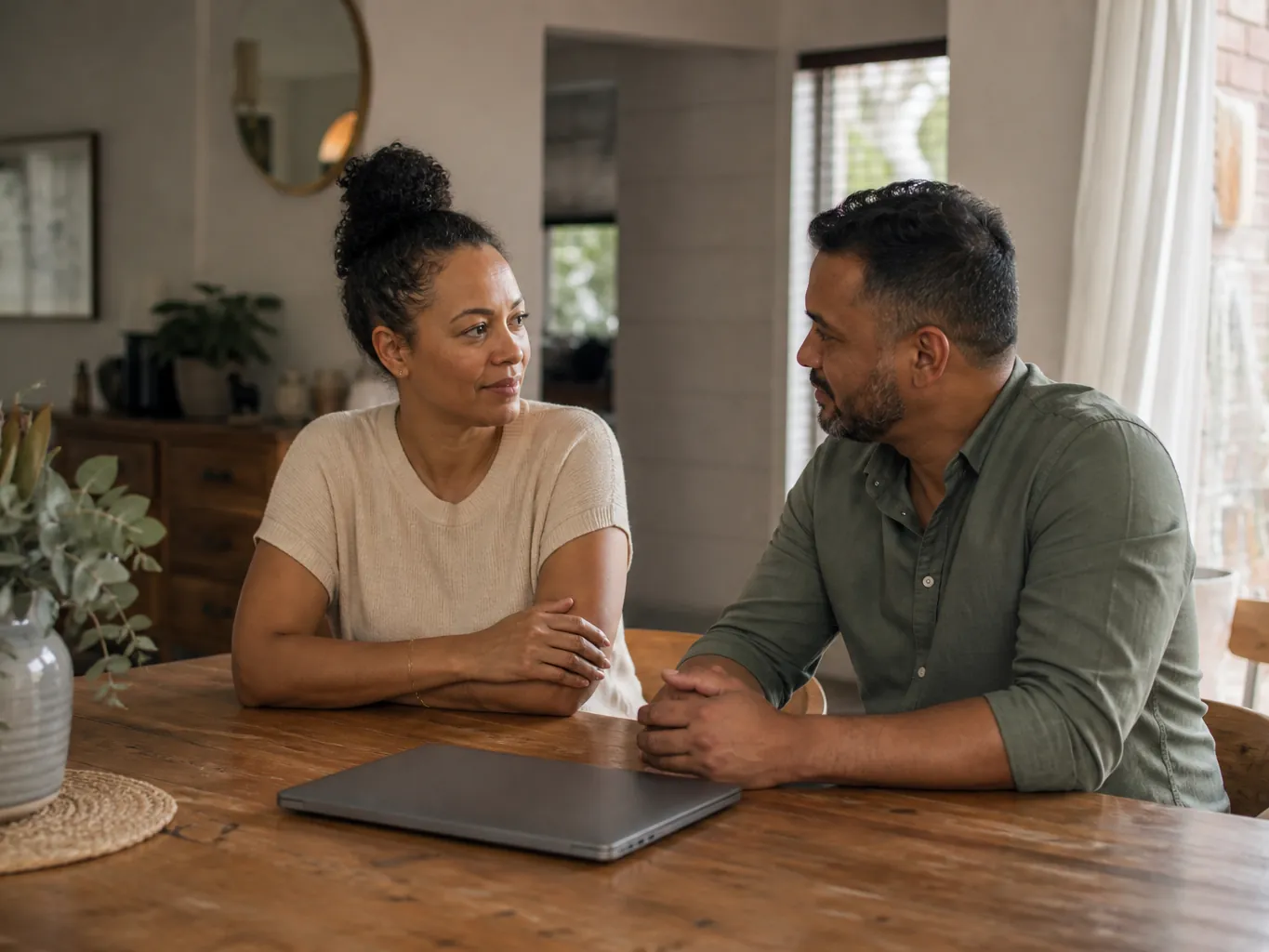 A couple talking at a dining table with a closed laptop